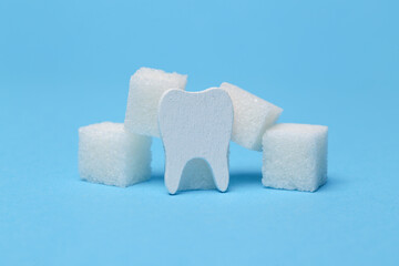 Tooth with sugar cubes on blue background. Harm of sugar and sweet for teeth, cause of caries