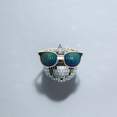 Minimal party concept. Sunglasses with disco ball on gray bright background. Top view