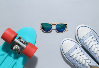 Hipster outfit on a gray background. Penny board with sunglasses and sneakers on a gray background....