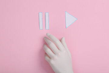 Obraz premium Plastic hand chooses between icons start, pause of media player on pink background.