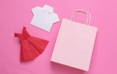 Shopping bag with origami dress and shirt on pink background. Shopping concept