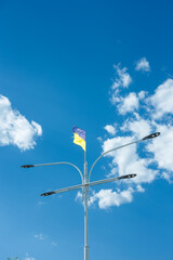 Ukrainian yellow and blue national flag on street lamp fluttering on blue cloudy sky background, vertical shot