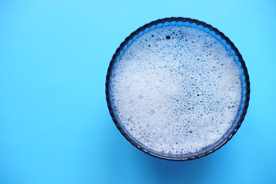 Glass bowl with foam water and bubbles on a blue table, copy space