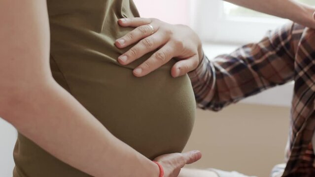 A Handsome Young Man Holds The Hand Of A Pregnant Woman In Labor. The Husband Supports His Wife While She Has Contractions And Breathes Together. Female With Pain In The Last Minutes Before Childbirth