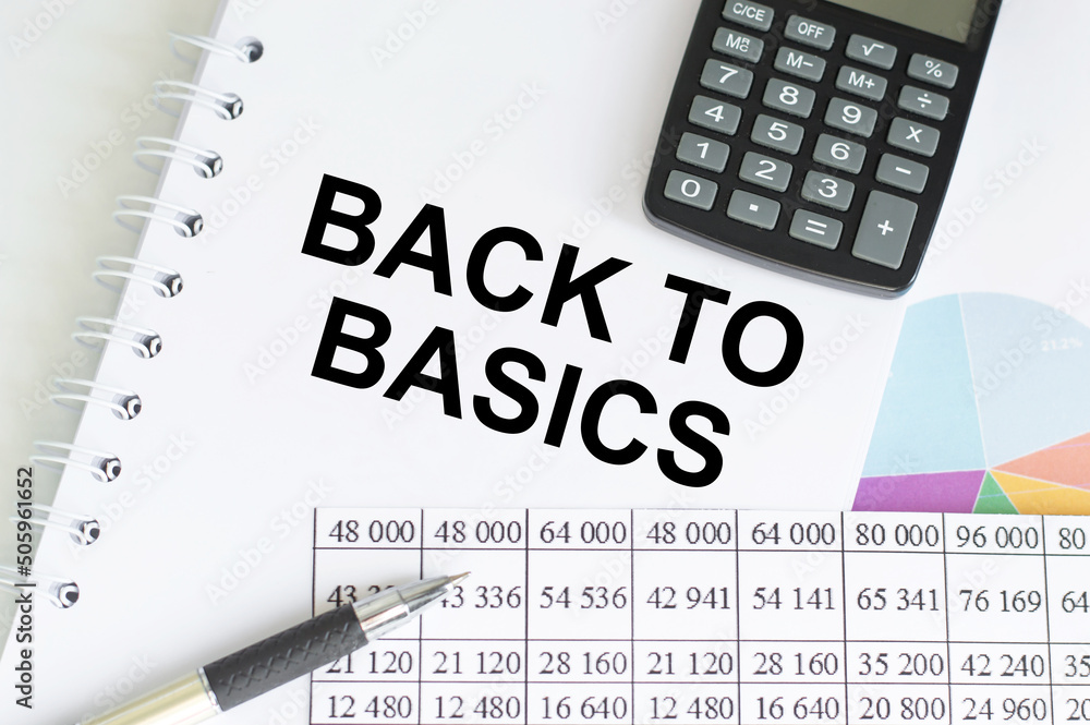 Aufkleber text back to basics on notepad on a table next to calculator, reports and charts