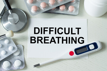 text DIFFICULT BREATHING on a white card on the table next to a thermometer, stethoscope and tablets, medical concept.