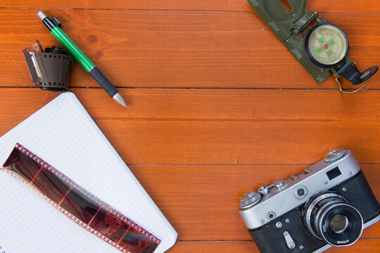 Photo camera, film, pen and compass lie on a wooden background.