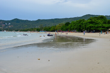 unrecognized people walking on beach in Thailand, water tide on sand, beach surrounded by green hills