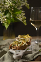 Bruschetta with gorgonzola cheese and pears, nuts on wooden table with textile, glass of white wine and beautiful flowers. Selective focus, copy space. 