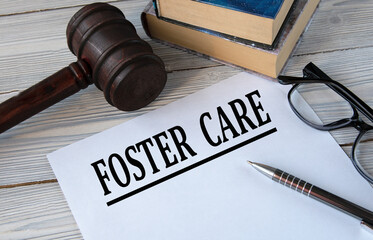 FOSTER CARE - words on white paper with the background of the judge's hammer, glasses and pen