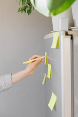 a woman makes notes on colored stickers on the refrigerator. a reminder or a note for her husband and children. home planning of tasks and a list of products to buy in the store. homemaker management