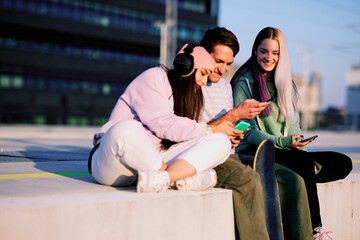 Three teenage friends are sitting in the urban exterior and hanging on their phones.