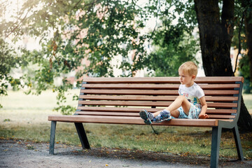 Little boy in summer city Park sitting on a bench.