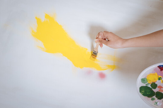 woman's hand applying yellow paint to canvas, close up shots