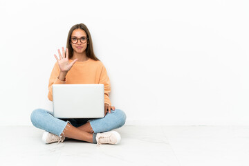 Young woman with a laptop sitting on the floor counting five with fingers