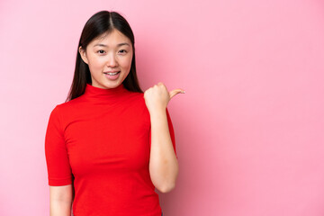 Young Chinese woman isolated on pink background pointing to the side to present a product