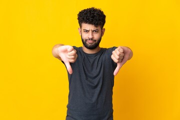 Young Moroccan man isolated on yellow background showing thumb down with two hands