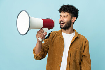 Young Moroccan man isolated on blue background holding a megaphone and smiling