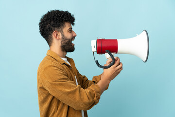 Young Moroccan man isolated on blue background shouting through a megaphone to announce something...