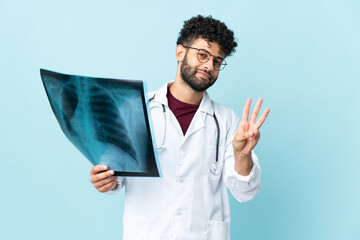 Young Moroccan traumatologist in workplace isolated on blue background happy and counting three with fingers