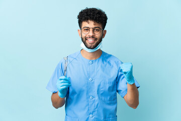 Moroccan dentist man holding tools isolated on blue background celebrating a victory in winner position