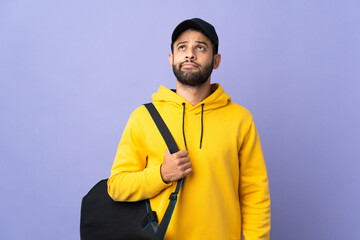 Young sport Moroccan man with sport bag isolated on purple background and looking up