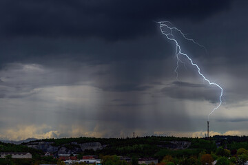 Lightning strikes a communications tower in the distance. Very dark clouds with heavy rain from...