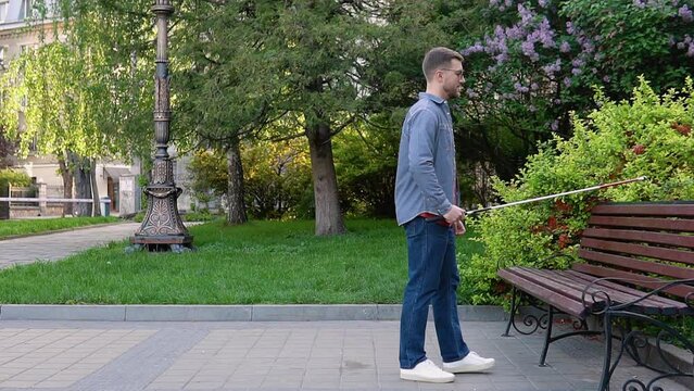 A blind man with a cane approaches the bench and sits down