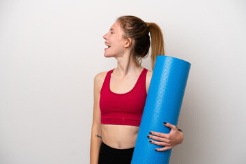 Young sport English woman going to yoga classes while holding a mat isolated on white background laughing in lateral position