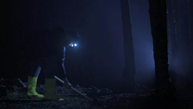 The man is digging in the forest. Night.
Man is digging the ground in the forest with a pickaxe. He's undercover, checking around.
