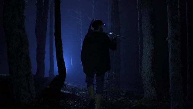 Man walking in the forest in the dark.  Man walking in the forest in the dark. He's got a pickaxe.
