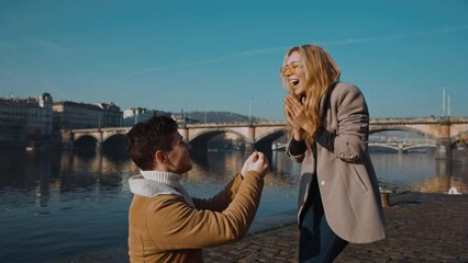 happy couple marriage proposal young man proposing to girlfriend with wedding ring enjoying surprise engagement. European town, pier, bridge on background