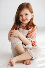 portrait of happy redhead baby girl sitting on the floor in sunny room. three years old