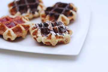 Waffles topped with chocolate and strawberries served in a white plate.