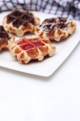Waffles topped with chocolate and strawberries served in a white plate.