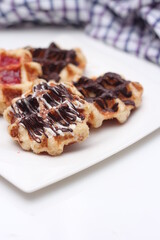 Waffles topped with chocolate and strawberries served in a white plate.