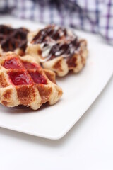 Waffles topped with chocolate and strawberries served in a white plate.