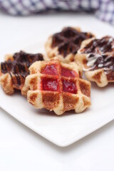 Waffles topped with chocolate and strawberries served in a white plate.