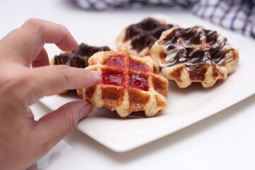 hand holding a waffle Garnish with chocolate and strawberries and serve in a white plate.