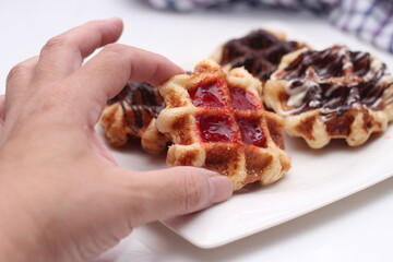 hand holding a waffle Garnish with chocolate and strawberries and serve in a white plate.