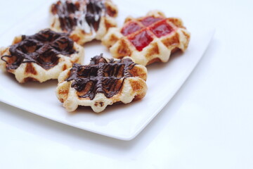 Waffles topped with chocolate and strawberries served in a white plate.