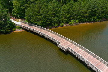 a long winding brown wooden bridge over a rippling silky green lake surrounded by lush green trees...