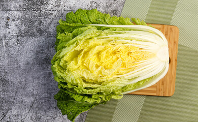 Half head of Napa Chinese cabbage on a wooden cutting board on a dark grey background. Top view,...