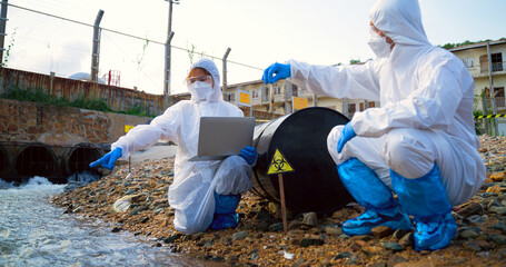 Team scientist in protective suit, mask and gloves collect sample of fish and dirty water from...