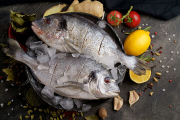Fresh ready to cook raw bream fish dorado with ingredients and seasonings like rosemary, salt, pepper, lime and olive oil, top view