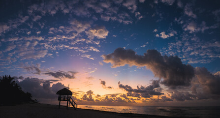 Sunrise over Playa del carmen Mexico along the sandy beach with a Lifeguard tower silhouetted against the sky