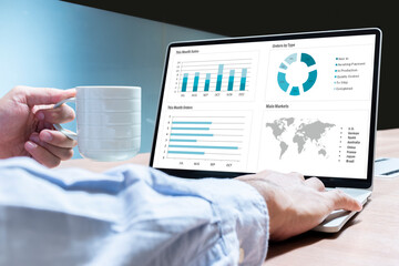 Businessman hand holding coffee cup with mockup chart presentation slide show on display laptop
