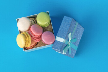 Top view of an open gift box with macaroon cookies on a blue background.