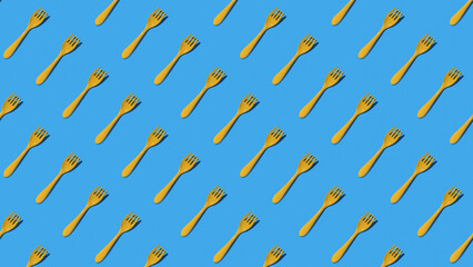 A pattern of yellow plastic forks on a blue background. Minimal concept.