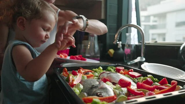 Mother teaches her little son how to cook healthy food in the kitchen. Lifestyle with caucasian people in single parent family. Child helps mother at kitchen.